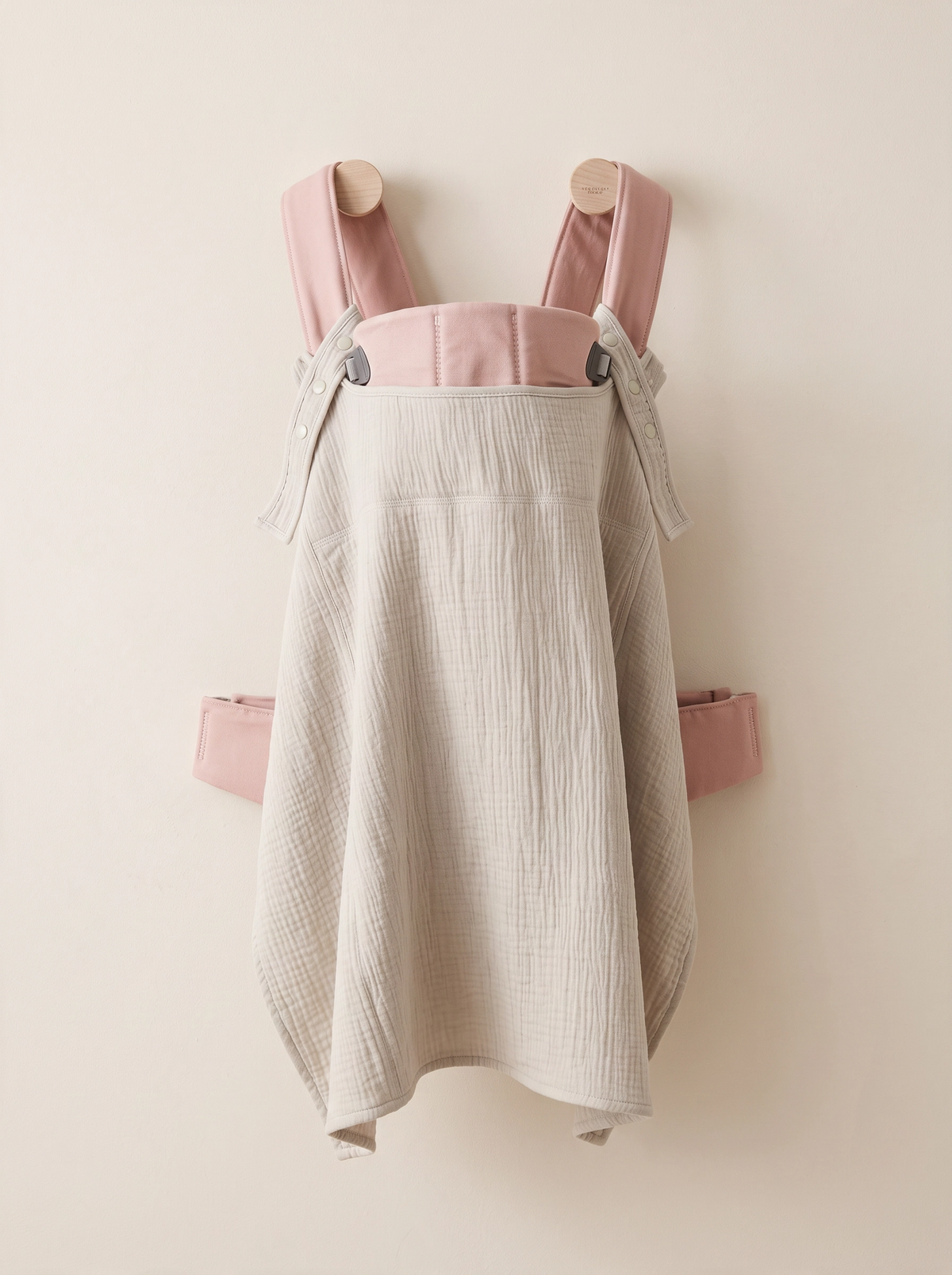 Sunshell sun cover in Sand, a light beige cotton cover for babywearing hanging from a pink baby carrier 